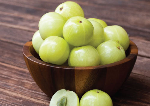 Wooden bowl filled with green Amla Berry fruits in a wooden bowl on a wooden surface