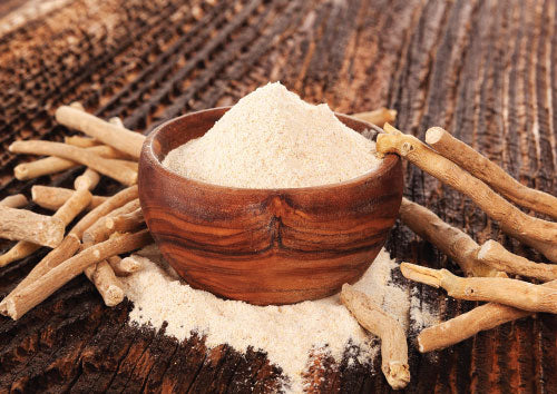 Wooden bowl filled with white Ashwaganda powder on a wooden surface with dried roots around.