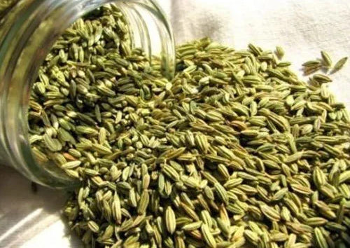 Green fennel seeds spilling out of a glass jar onto a white cloth.