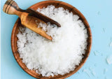 white magnesium flakes in brown wooden bowl with wooden scoop sitting on blue surface