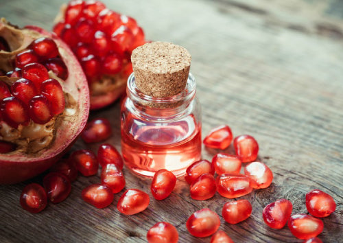 Clear glass jar with cork top filled with red liquid sitting on wooden surface next to Pomegranate Seeds
