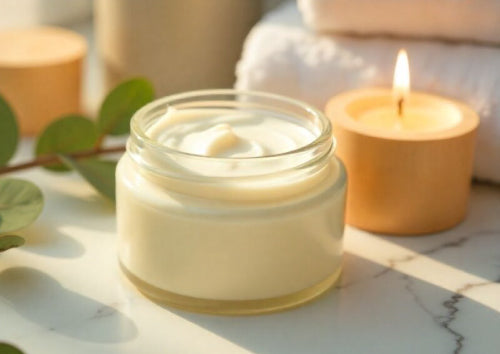 Jar of tallow cream on a marble surface with a lit candle and eucalyptus leaves.