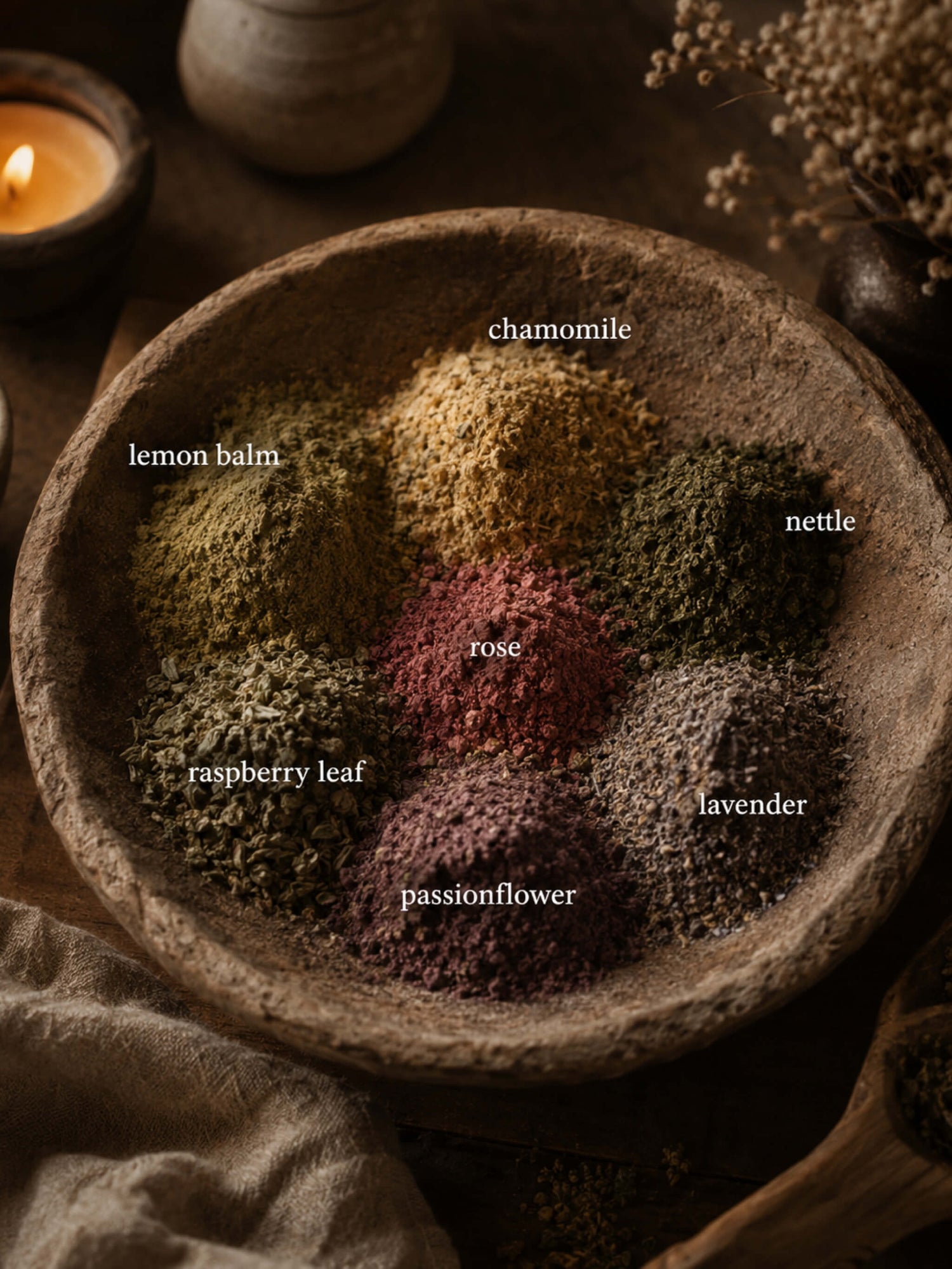 A rustic stone bowl filled with six labeled loose herbal powder blends: chamomile, lemon balm, nettle, raspberry leaf, lavender, and passionflower, arranged in a circular pattern on a dark wooden surface with a candle and dried flowers in the background.