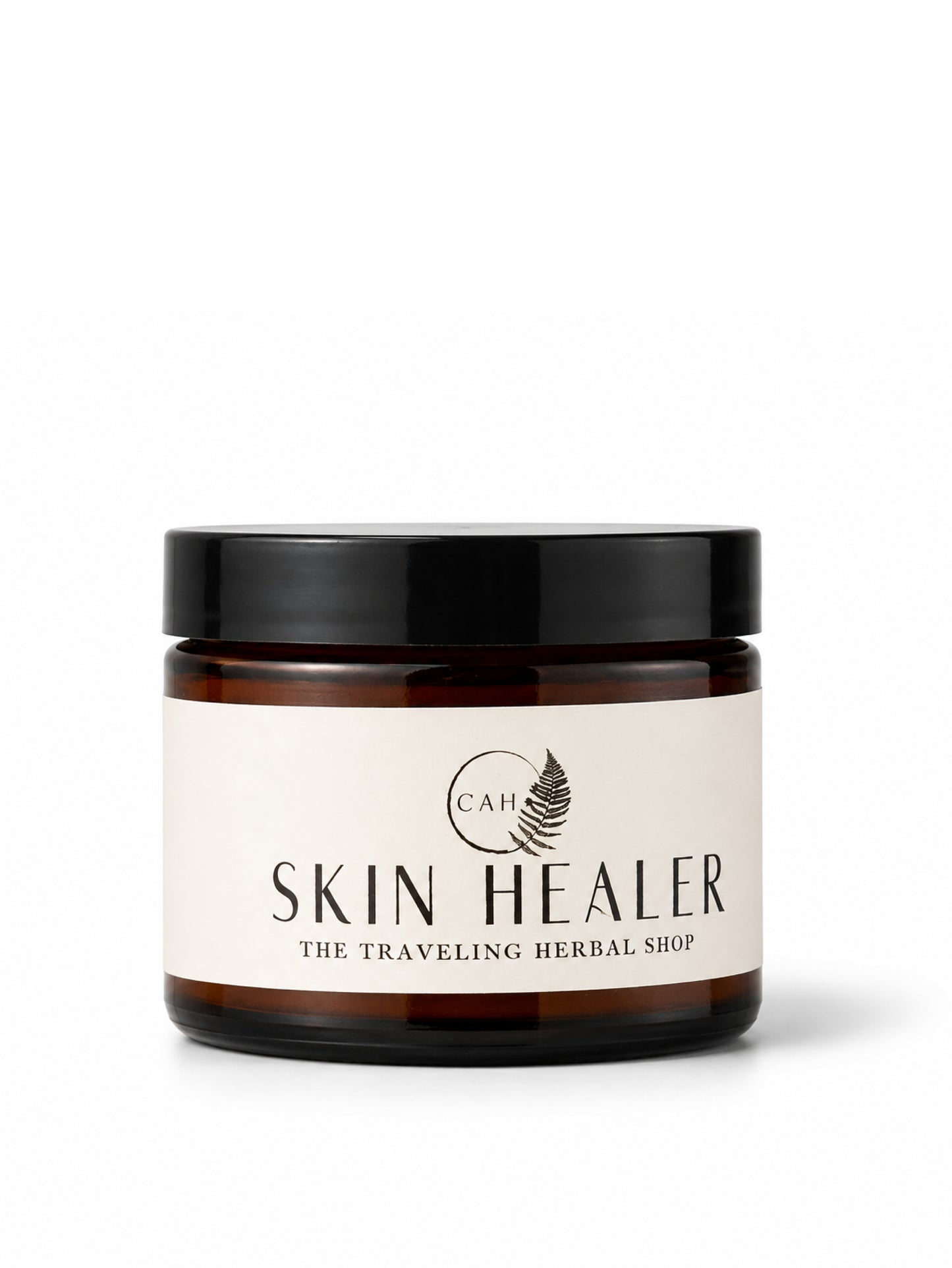 An amber glass jar with a black lid and a cream-colored label reading 'SKIN HEALER' and 'THE TRAVELING HERBAL SHOP', on a white background.
