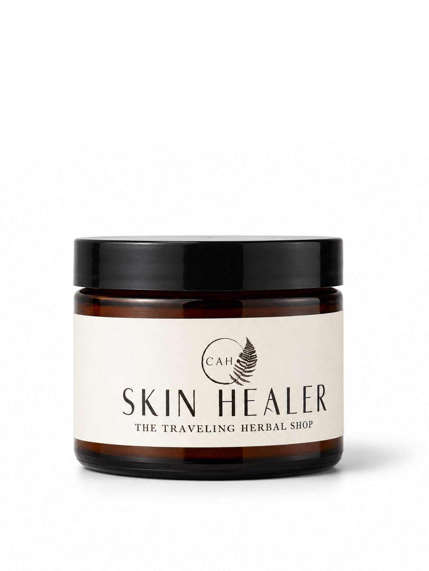 An amber glass jar with a black lid and a cream-colored label reading 'SKIN HEALER' and 'THE TRAVELING HERBAL SHOP', on a white background.